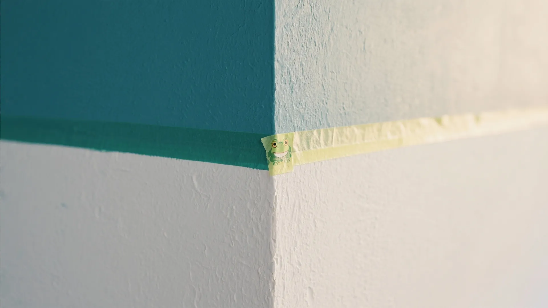 Macro view of a crisp tape line between a deep teal paint band and warm white on a big wall design.