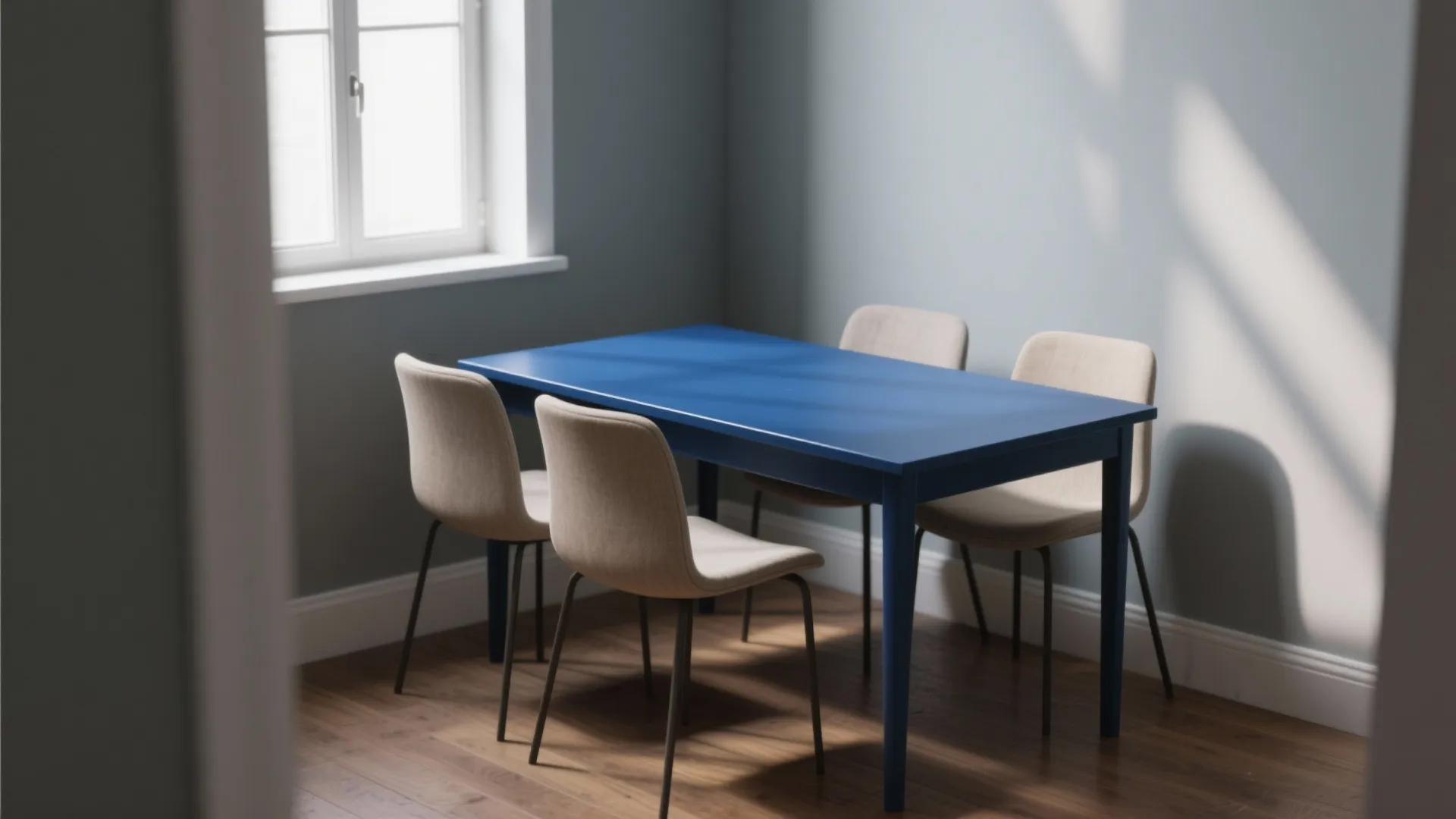 Simple rectangular blue wooden dining table with four beige chairs in a minimalist grey room