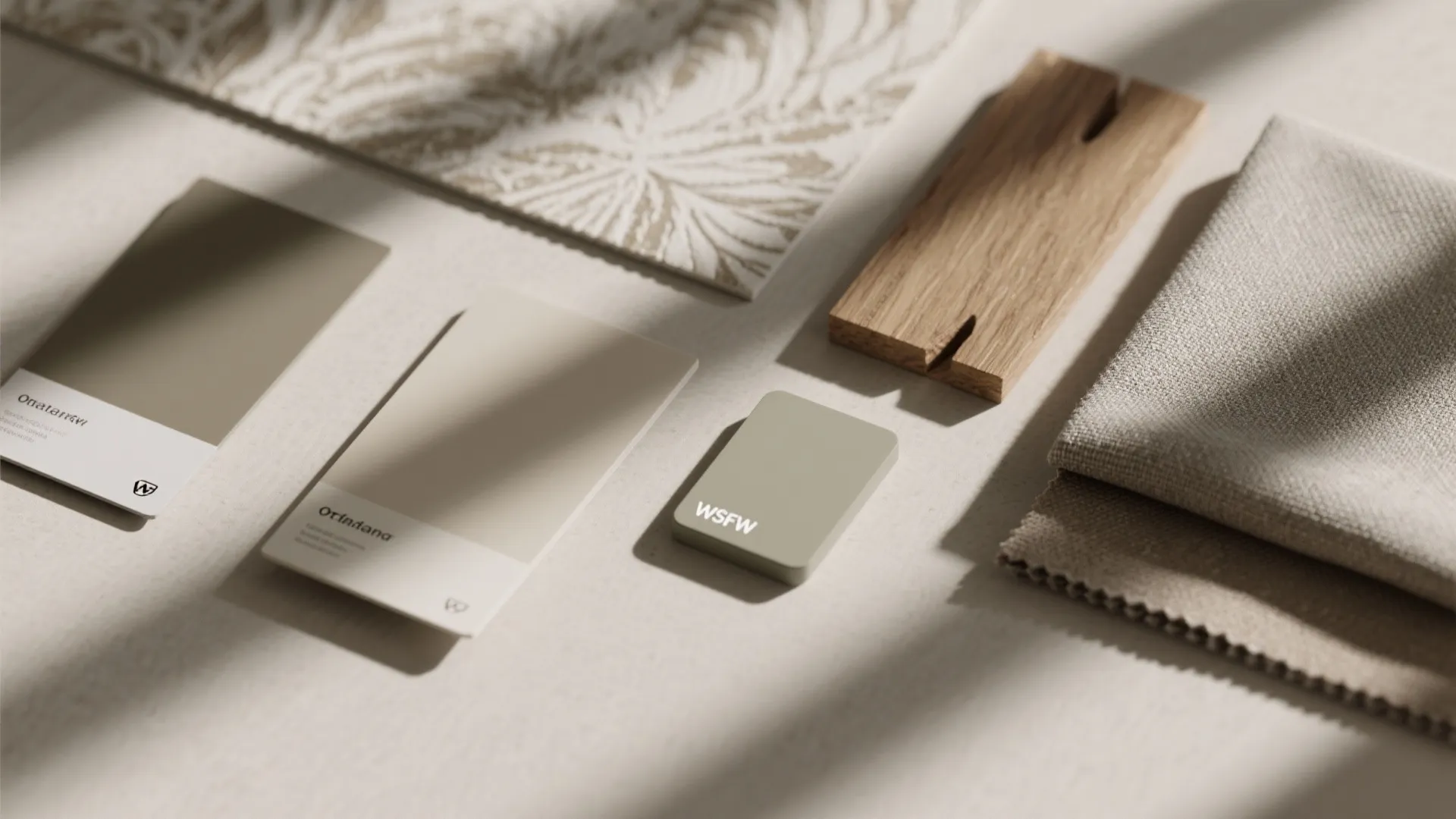 Top-down view of paint swatches, textured wallpaper and fabric samples showing a restrained palette with texture.