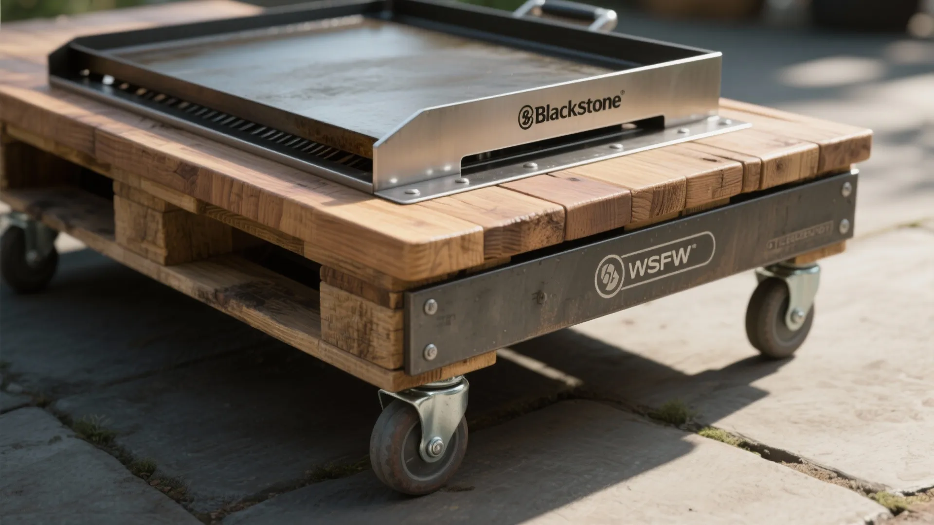 Metal outdoor cooking griddle placed on a wooden pallet base with four small black wheels