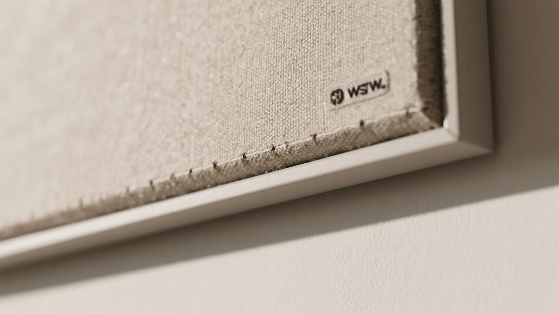 Close-up of a beige fabric wall panel with visible stitching details and a small logo