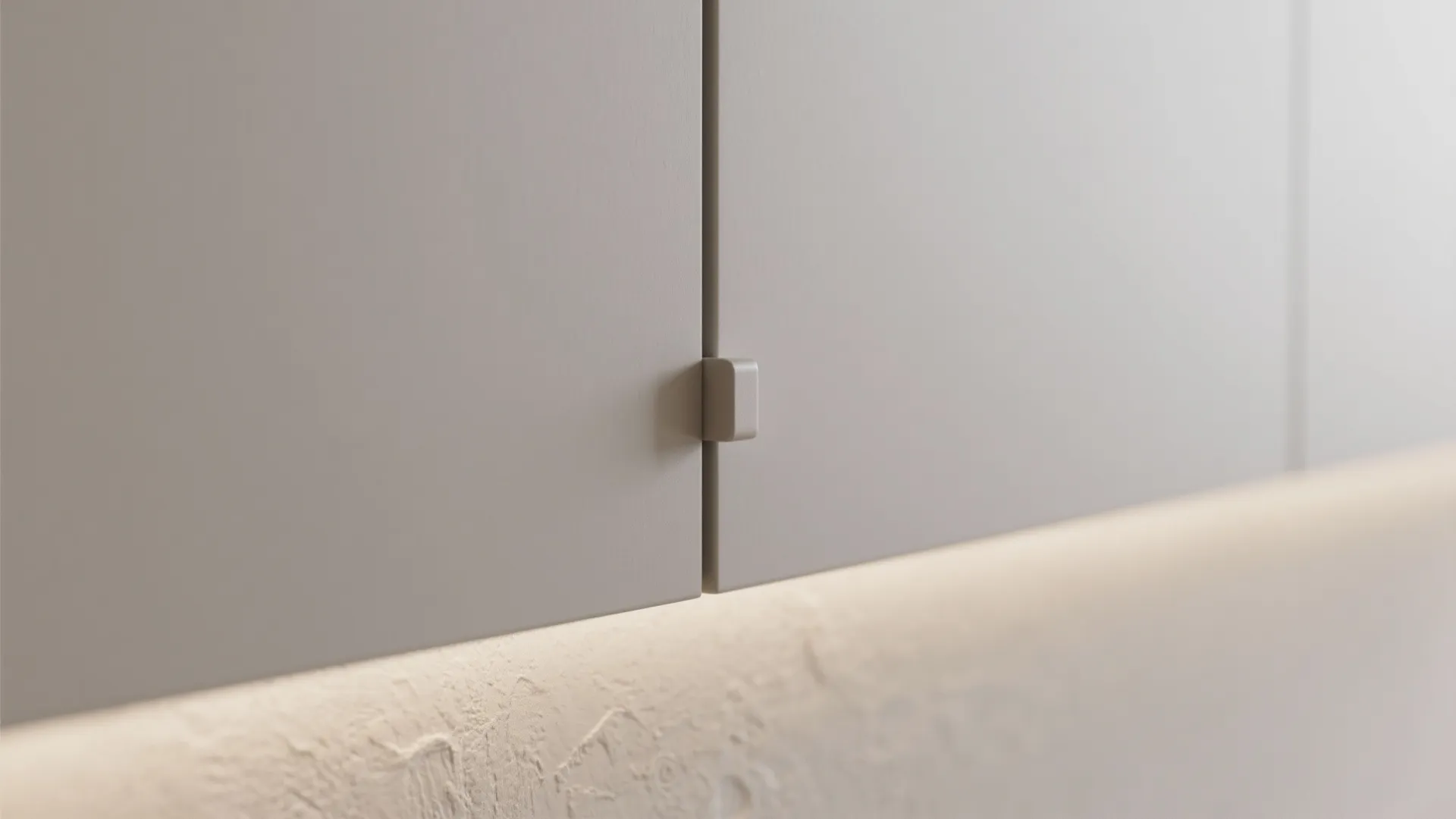 Close up of grey cabinet doors with small square handle and warm hidden light below
