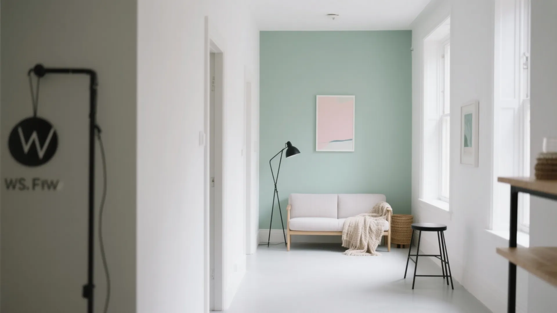 Modern white hallway with light green accent wall, simple grey sofa, floor lamp, and artwork
