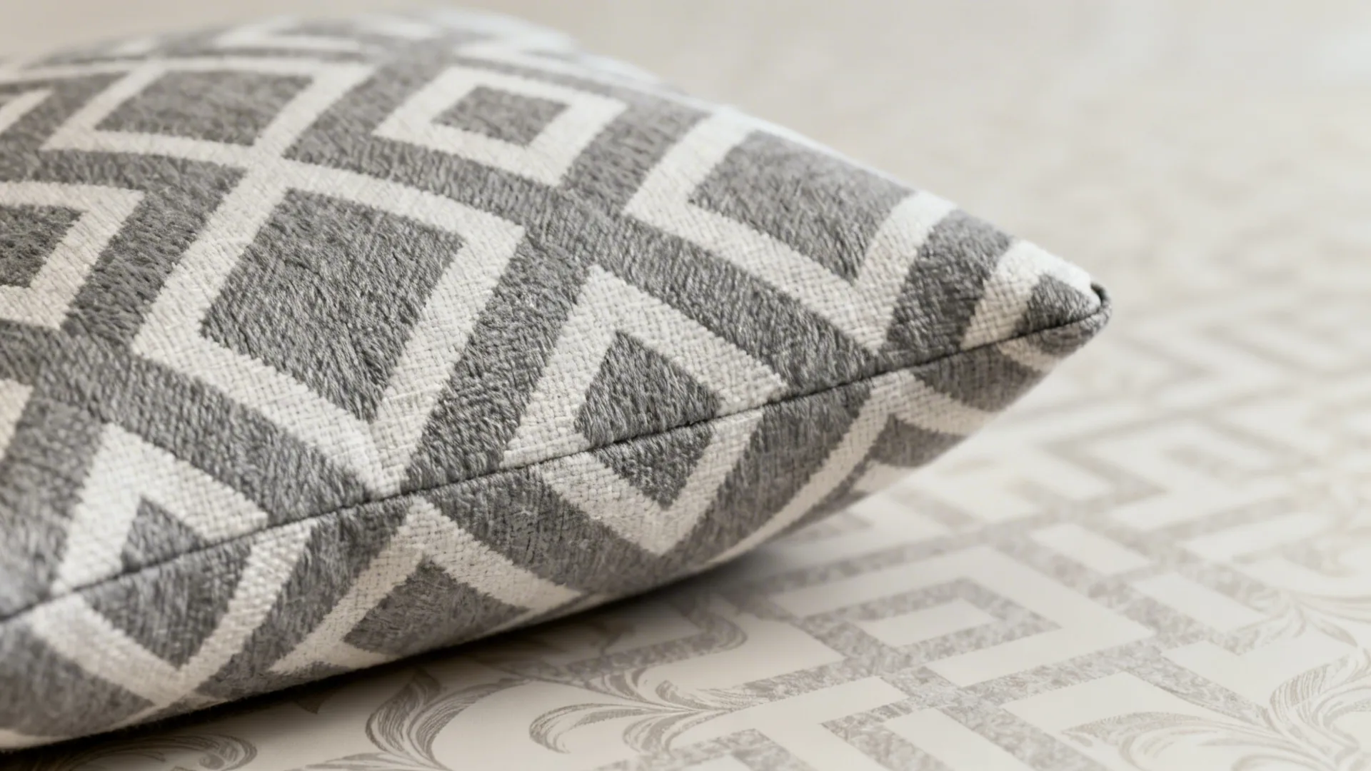 Close-up of subtle grey-and-white geometric cushion pattern and wallpaper texture.