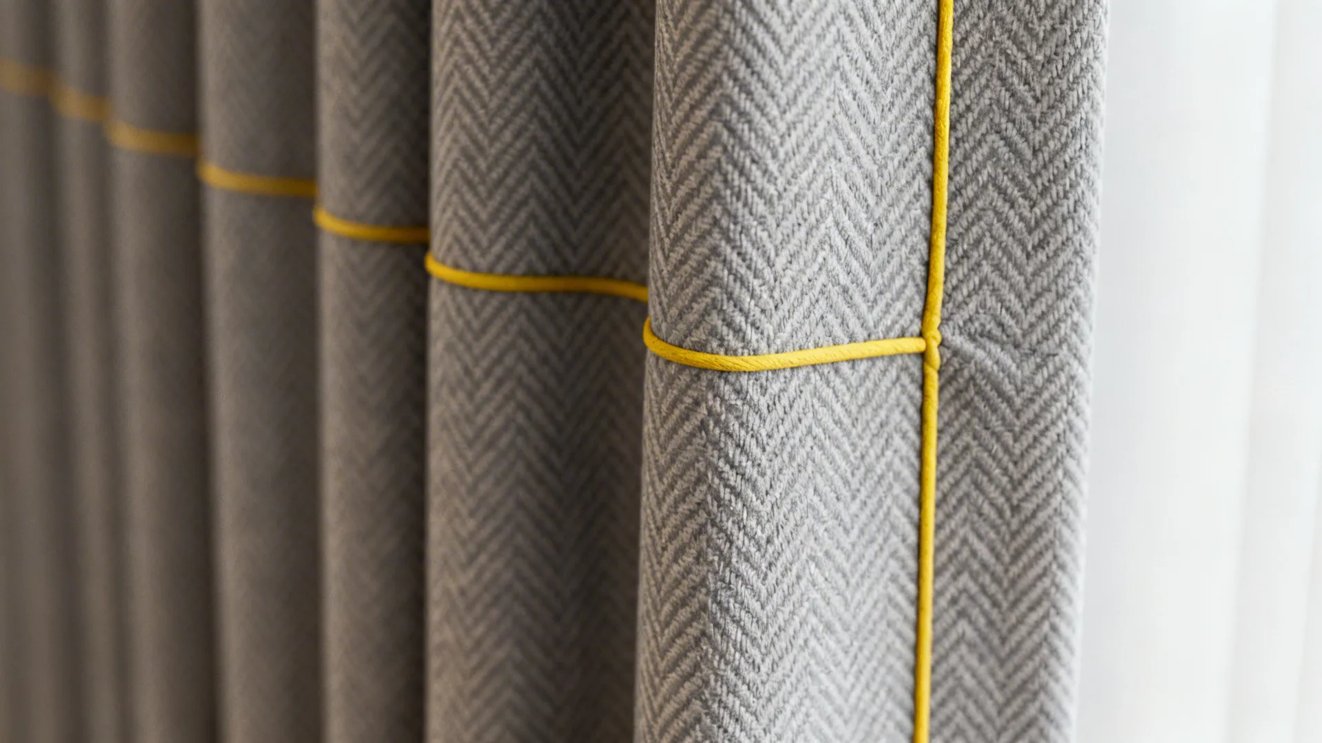Close-up of patterned gray curtain fabric with neat yellow piping along the edge.