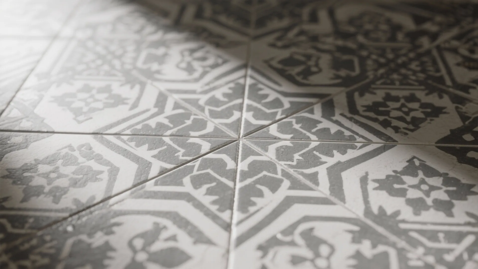 Close up of patterned grey and white floor tiles with geometric flower designs under soft sunlight