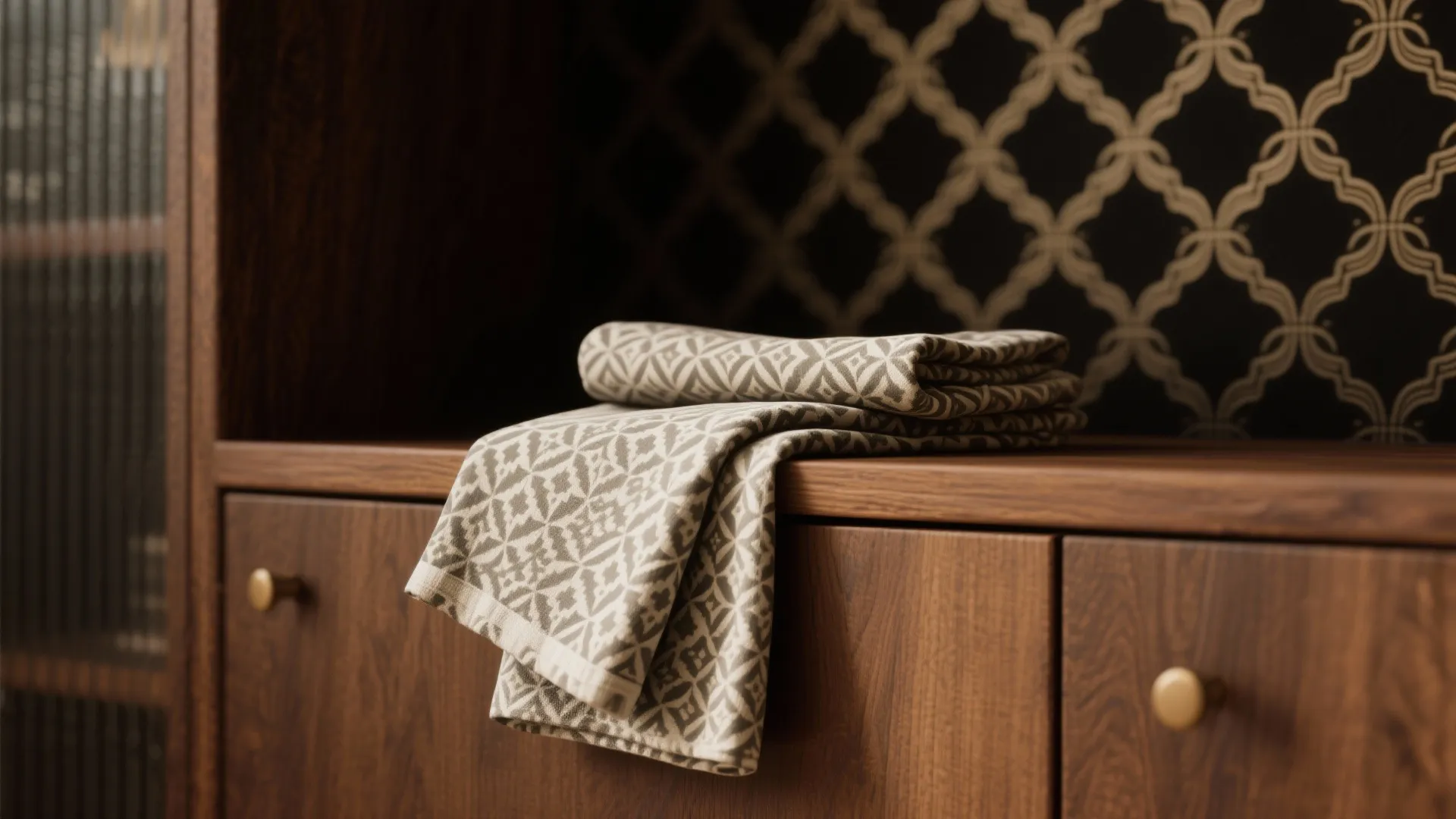 Folded patterned cloth resting on wooden cabinet with dark wallpaper background in a home setting