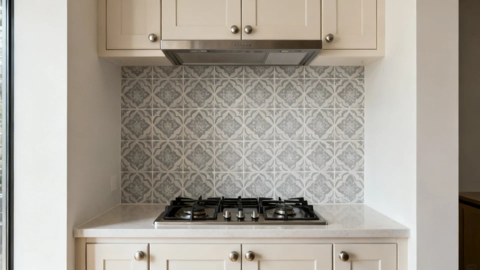 Soft-gray Moroccan-inspired patterned porcelain tile panel behind a cooktop in a small kitchen.