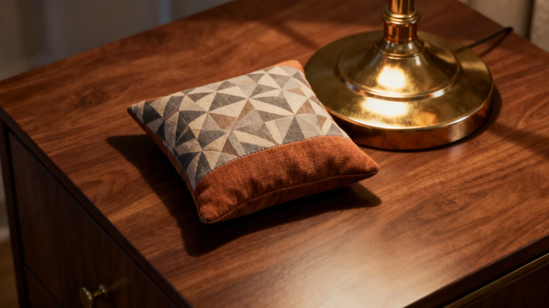 Geometric pillow and brass lamp on a walnut table adding subtle pattern and shine