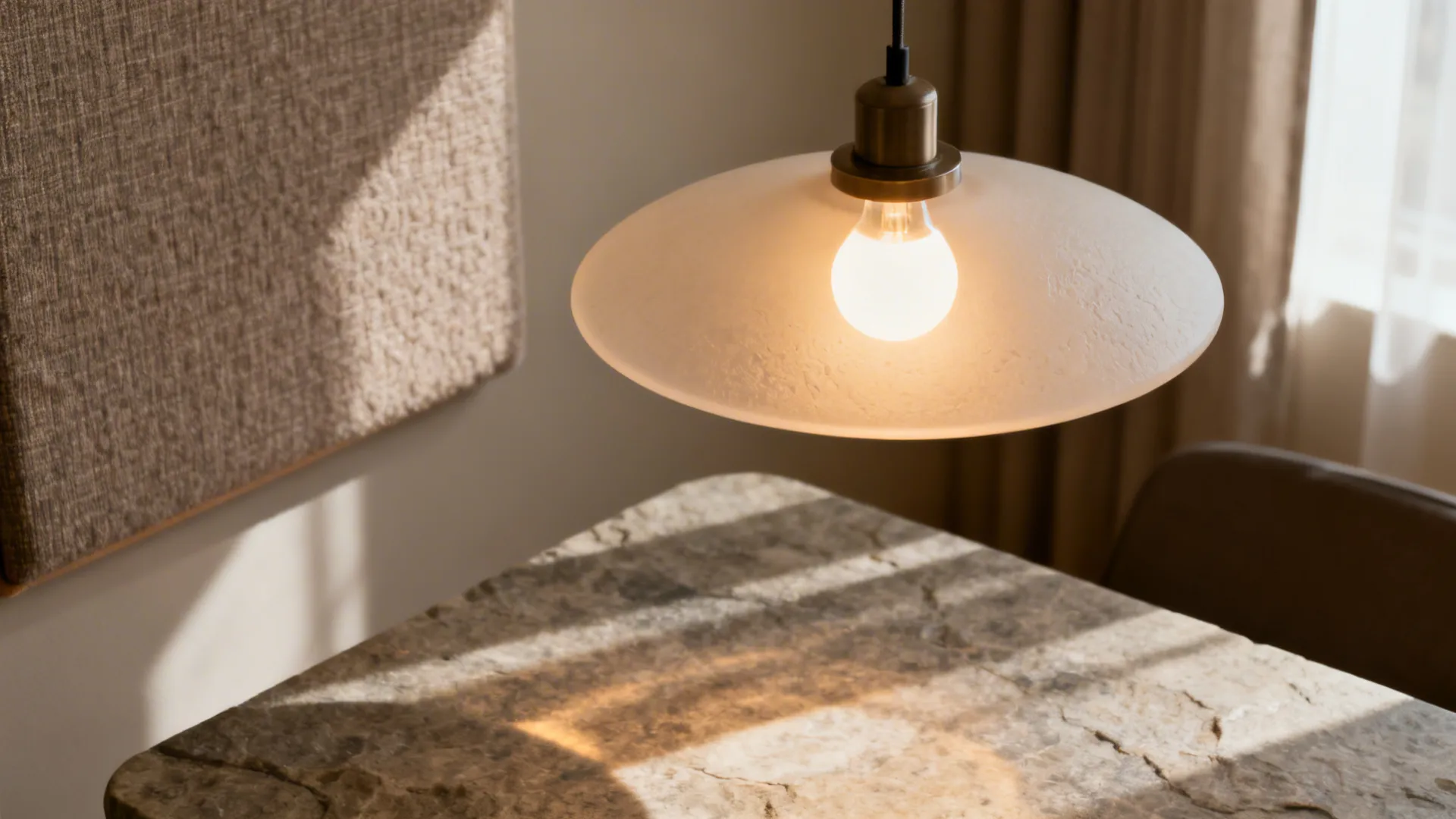 Close-up of a diffused pendant light with soft glow and nearby textile panel for acoustic comfort.