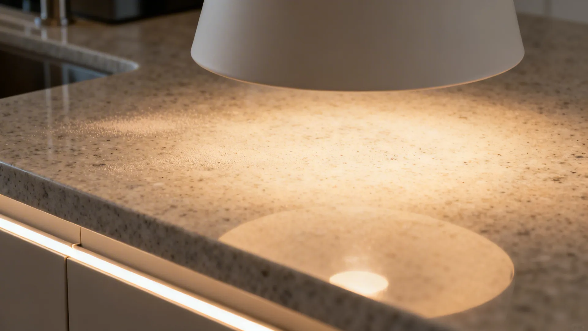 Close up of a white light fixture shining warm light onto a speckled granite kitchen countertop