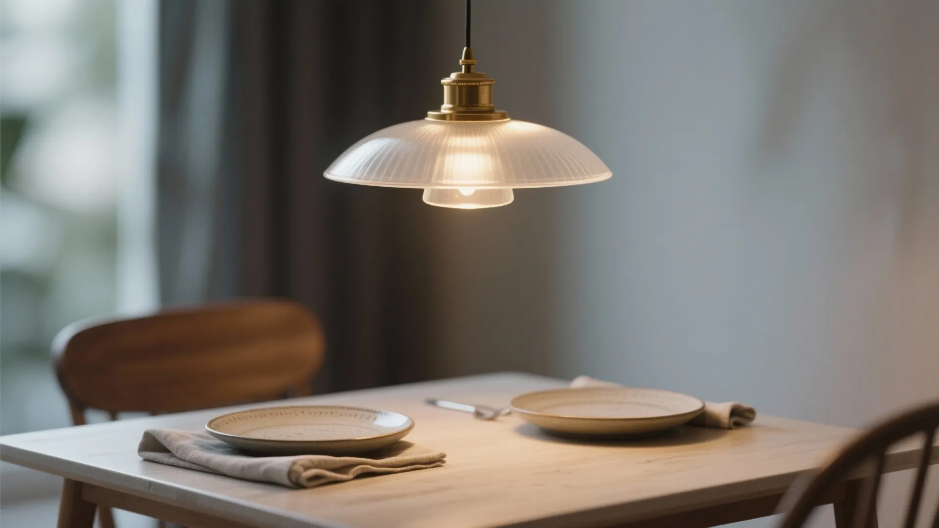 Glass ceiling light hanging over a wooden dining table with two plates and beige napkins