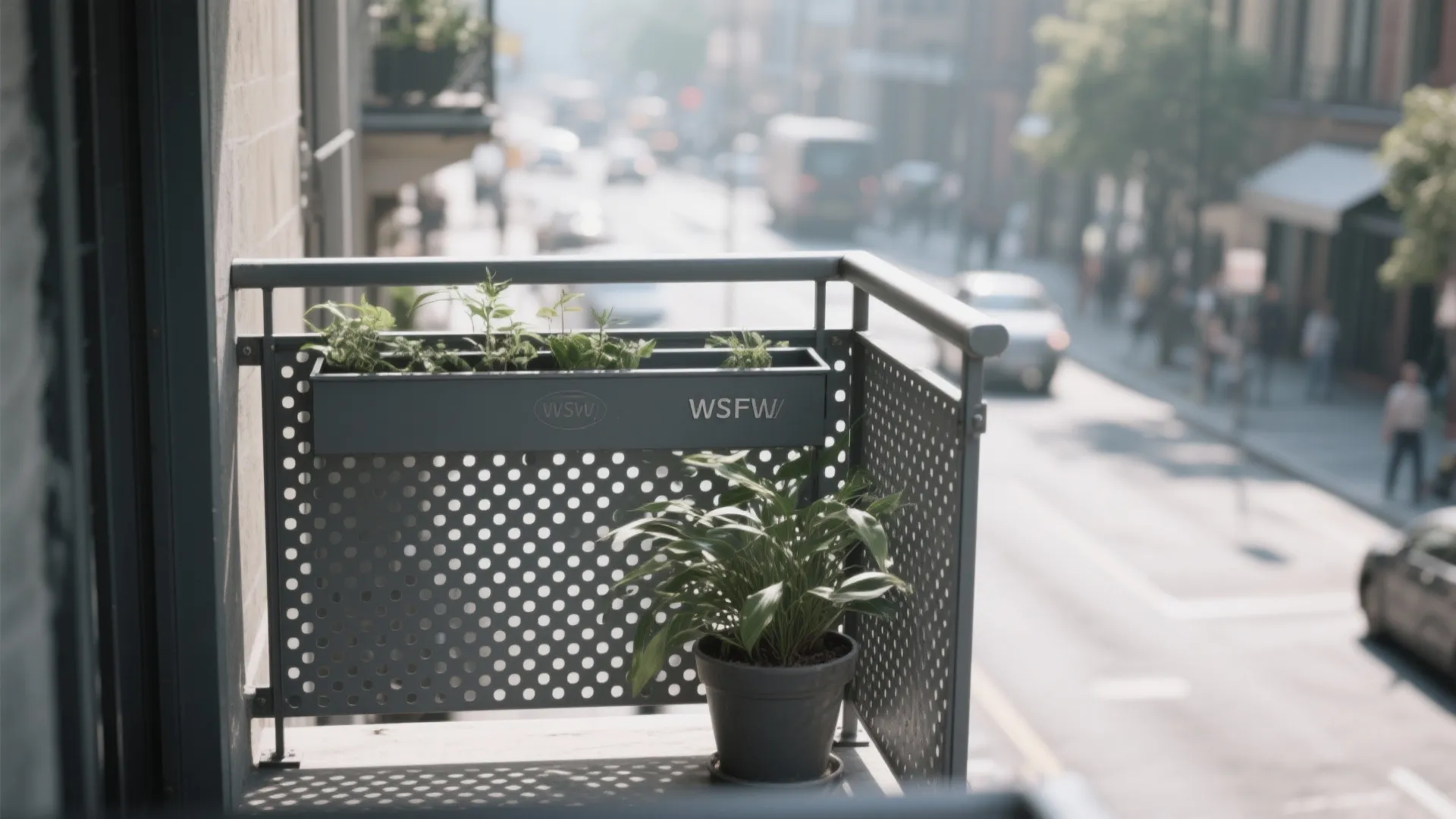 Grey metal balcony railing with small round holes featuring green plants overlooking a city street