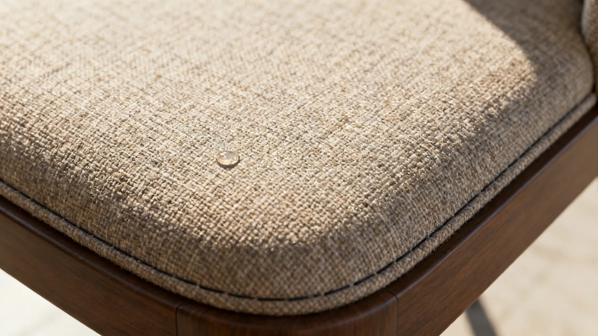 Close up of a single water drop sitting on a beige textured fabric chair cushion