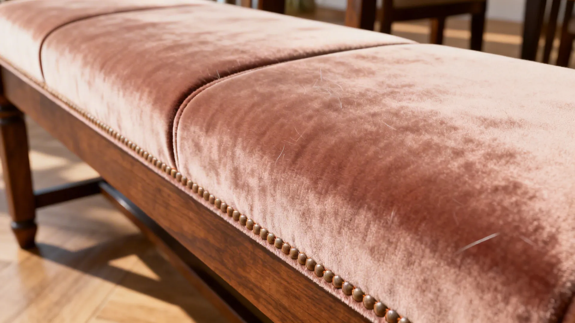 Close up of a pink velvet bench with wooden legs and decorative metal nailhead trim