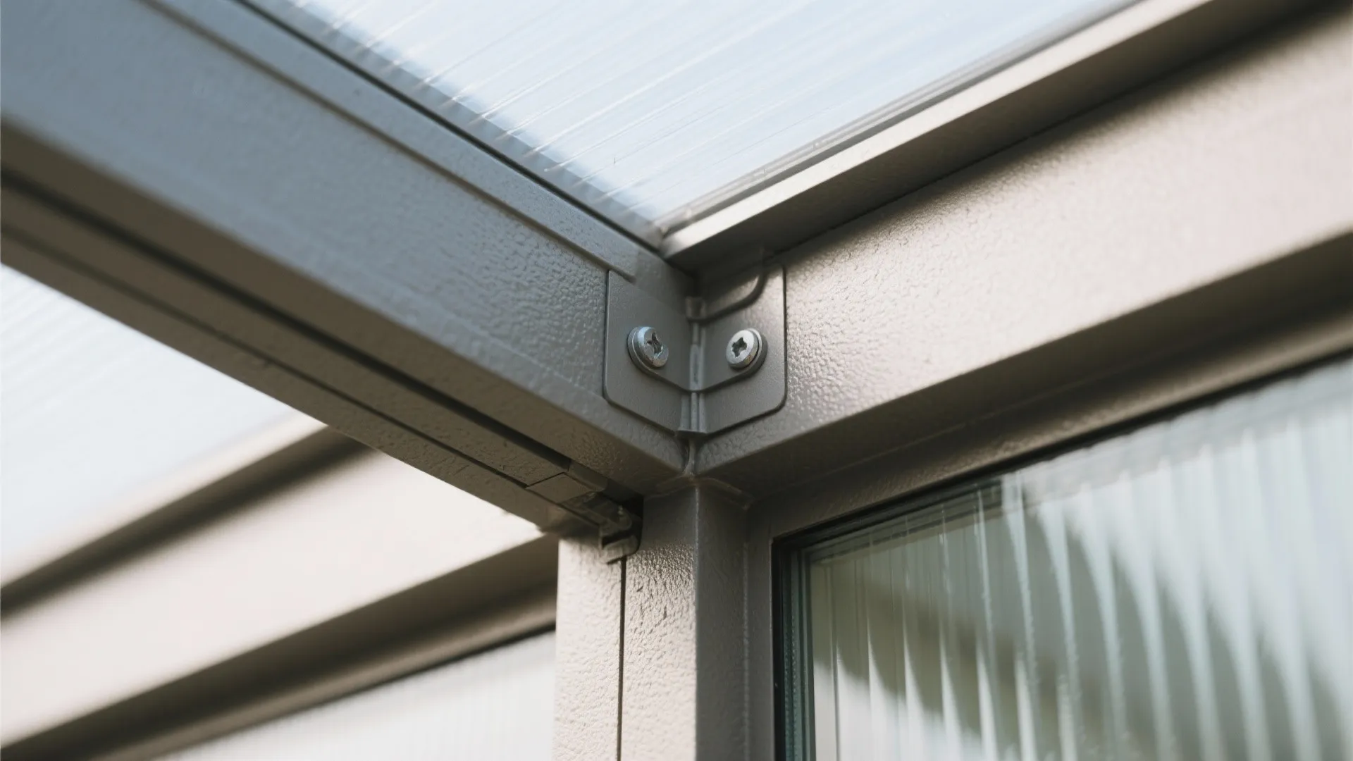 Close-up of a grey metal frame joint with screws holding a clear glass roof panel