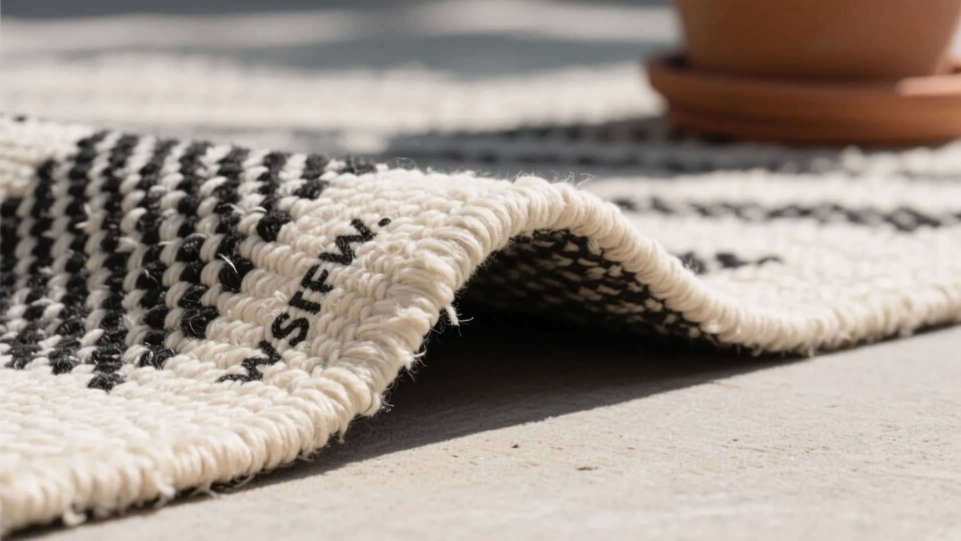 Macro of recycled PET outdoor flatweave rug edge in black and ecru with low-pile texture.
