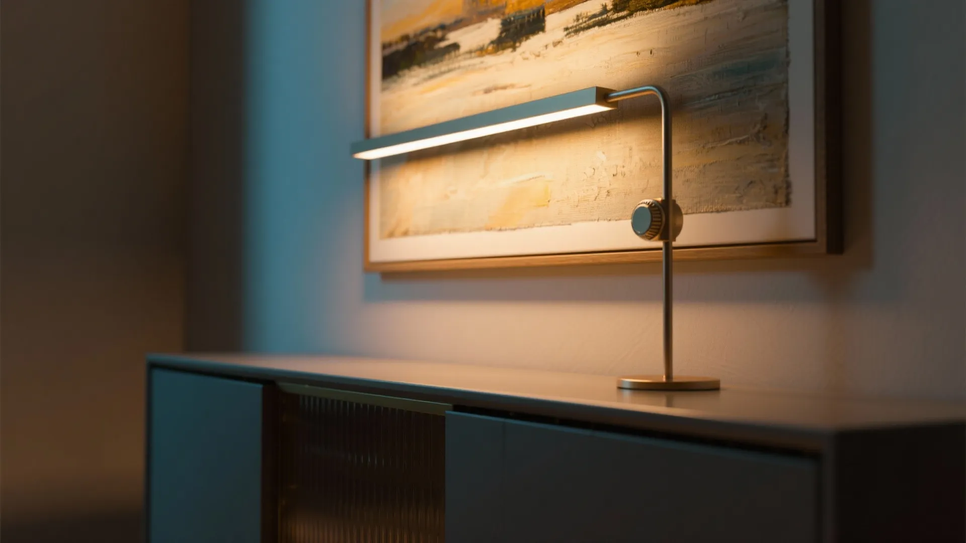 Modern gold wall light shining on framed art above a grey cabinet in warm room