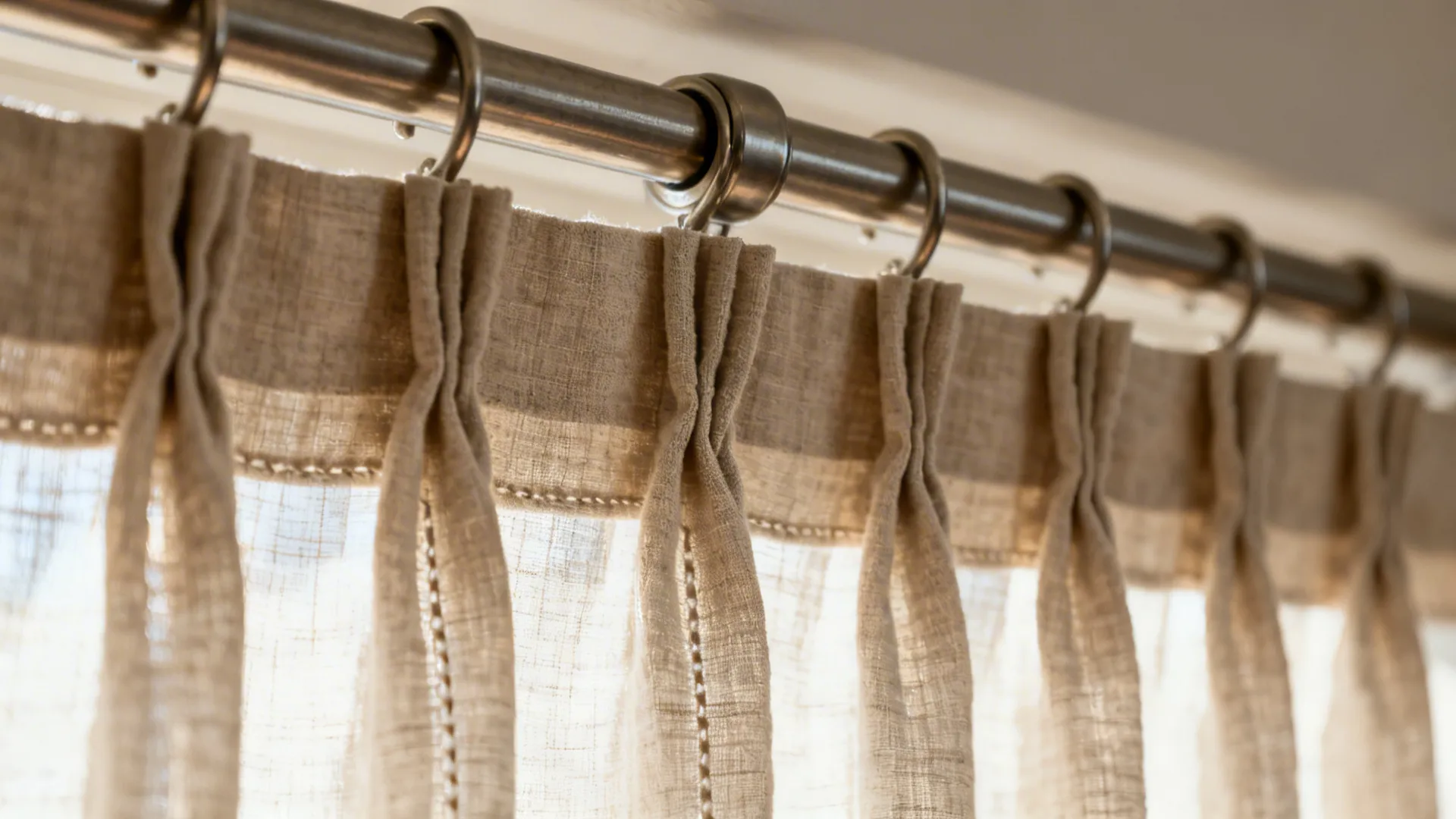 Macro view of pinch-pleat linen drapery on a continuous rod with center support.