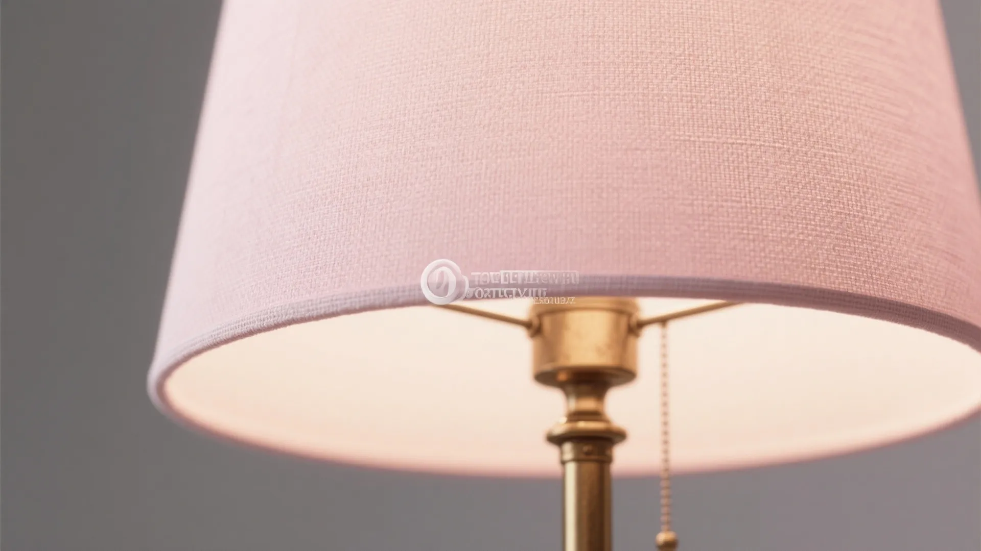Close-up of a light pink linen lampshade on a brushed brass base showing fabric texture and warm light diffusion.