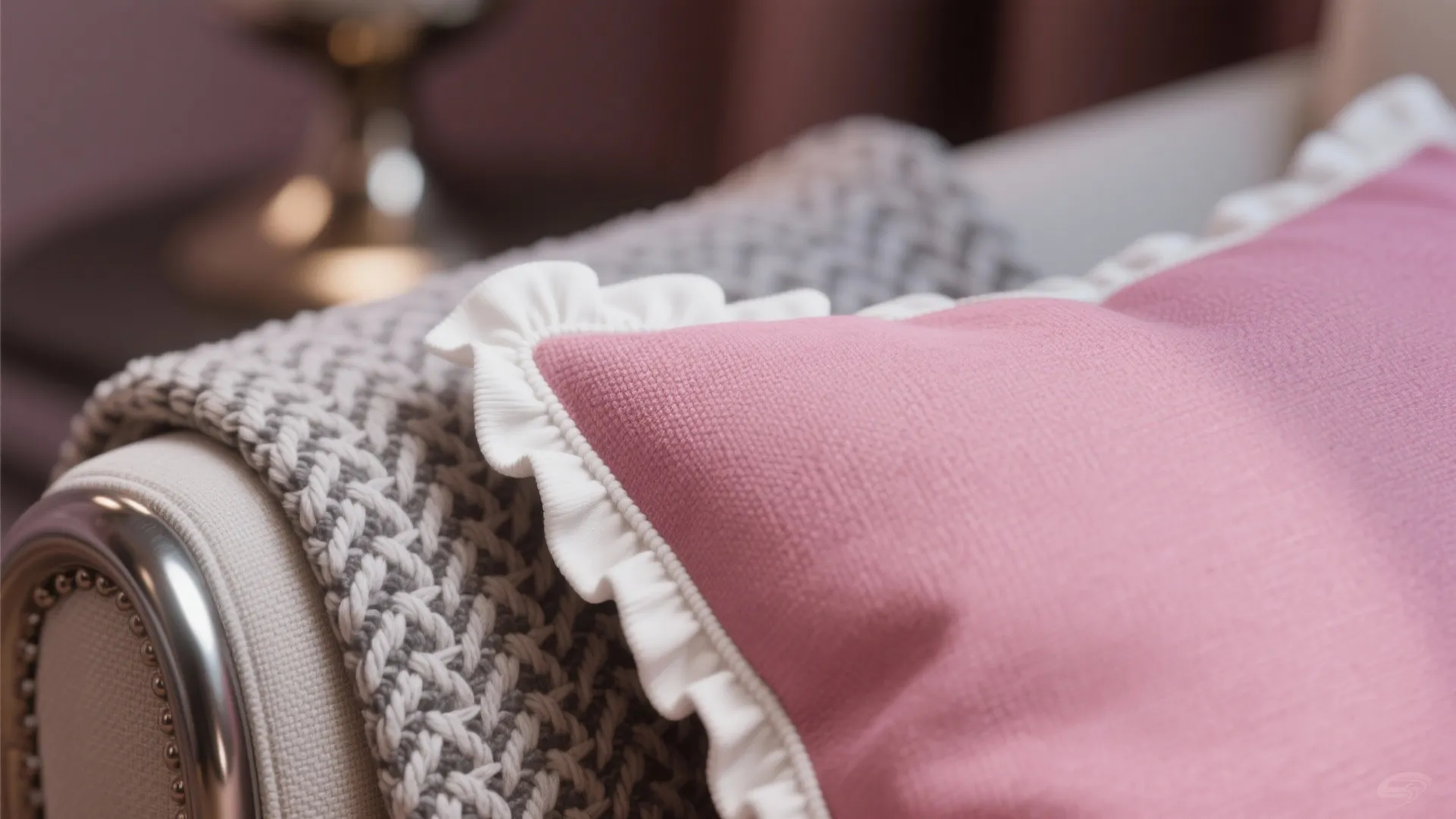 Close up of a pink pillow with white frills placed on a grey textured blanket