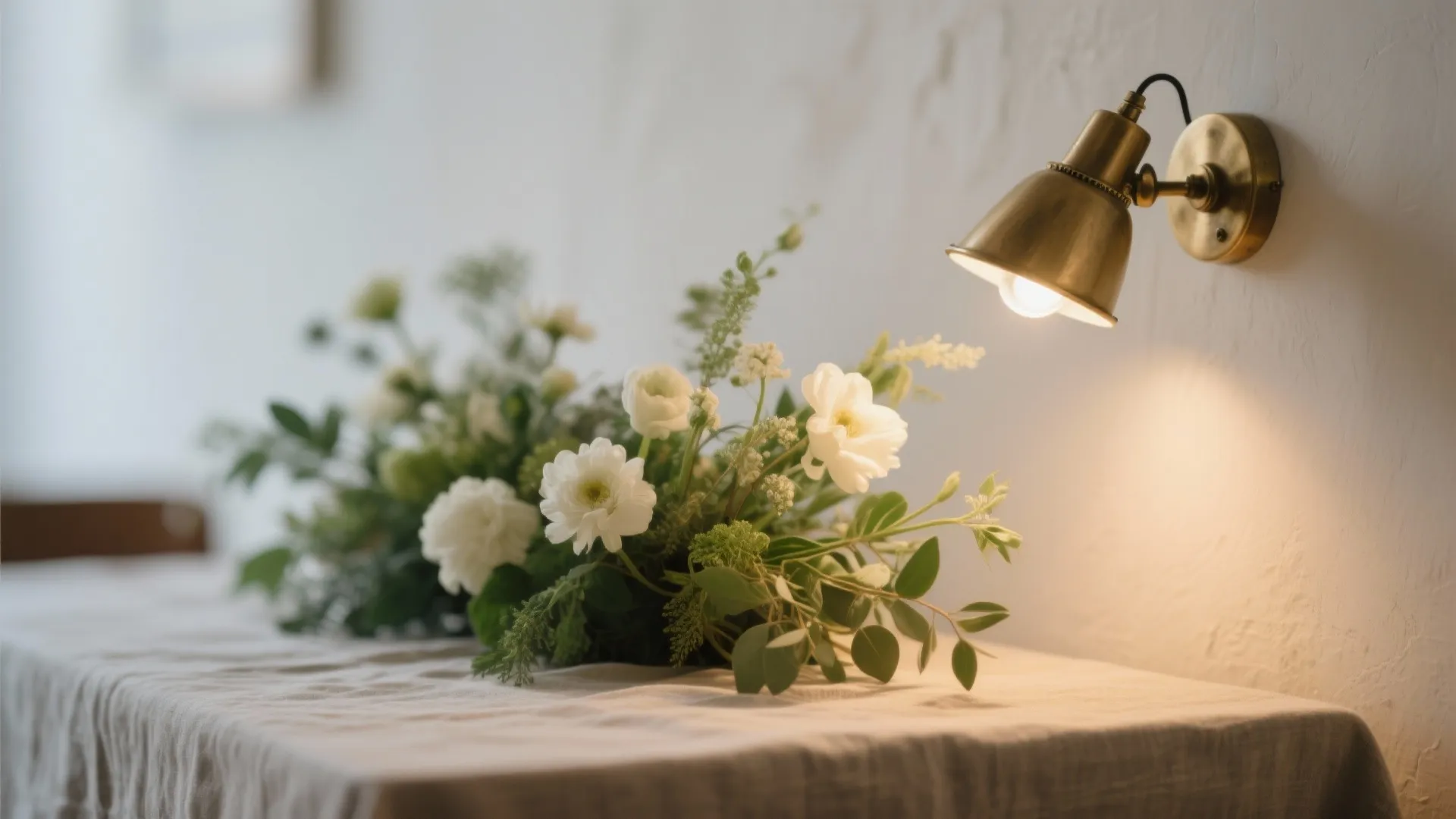 Close up view of white flowers on a table with a brass wall light fixture