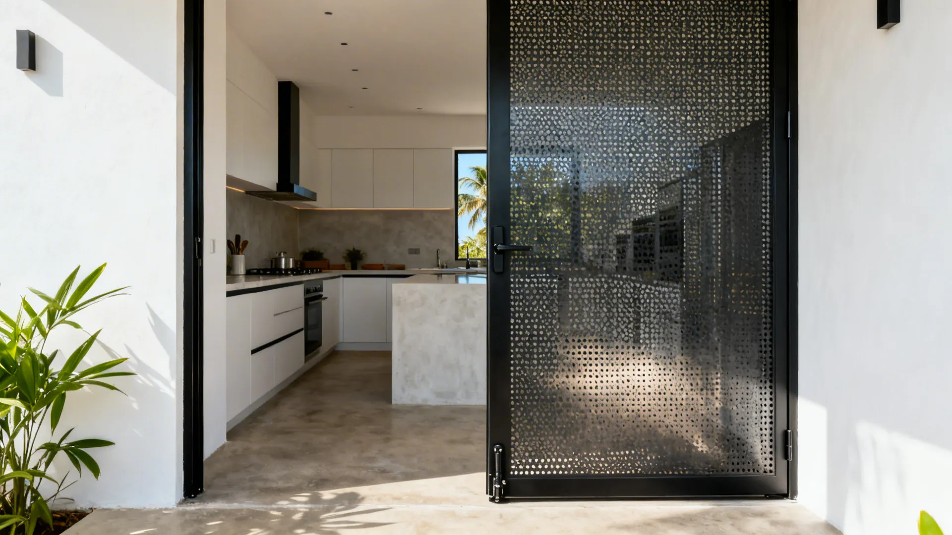 Slim black metal pivot kitchen door with micro-perforated panel in a coastal Kerala home.