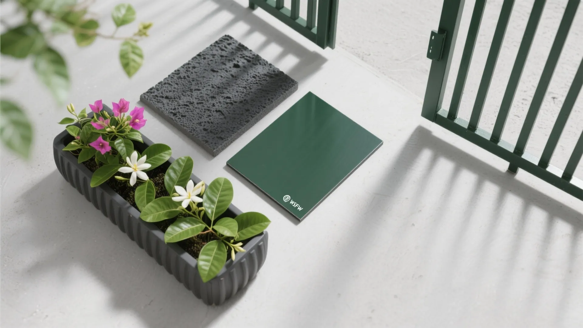 Planter with pink and white flowers next to stone and green material samples by gate