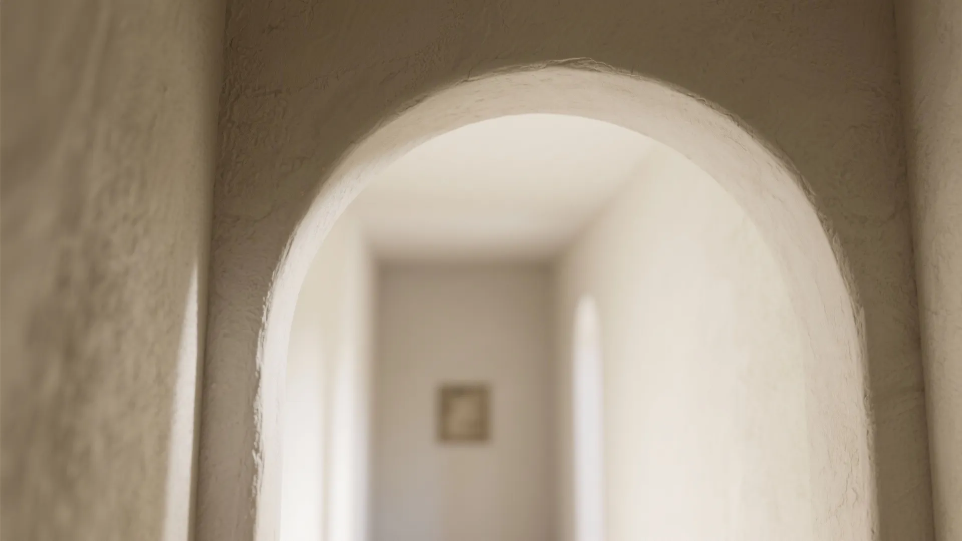 Close up view of a white plaster arched doorway leading into a bright minimalist hallway
