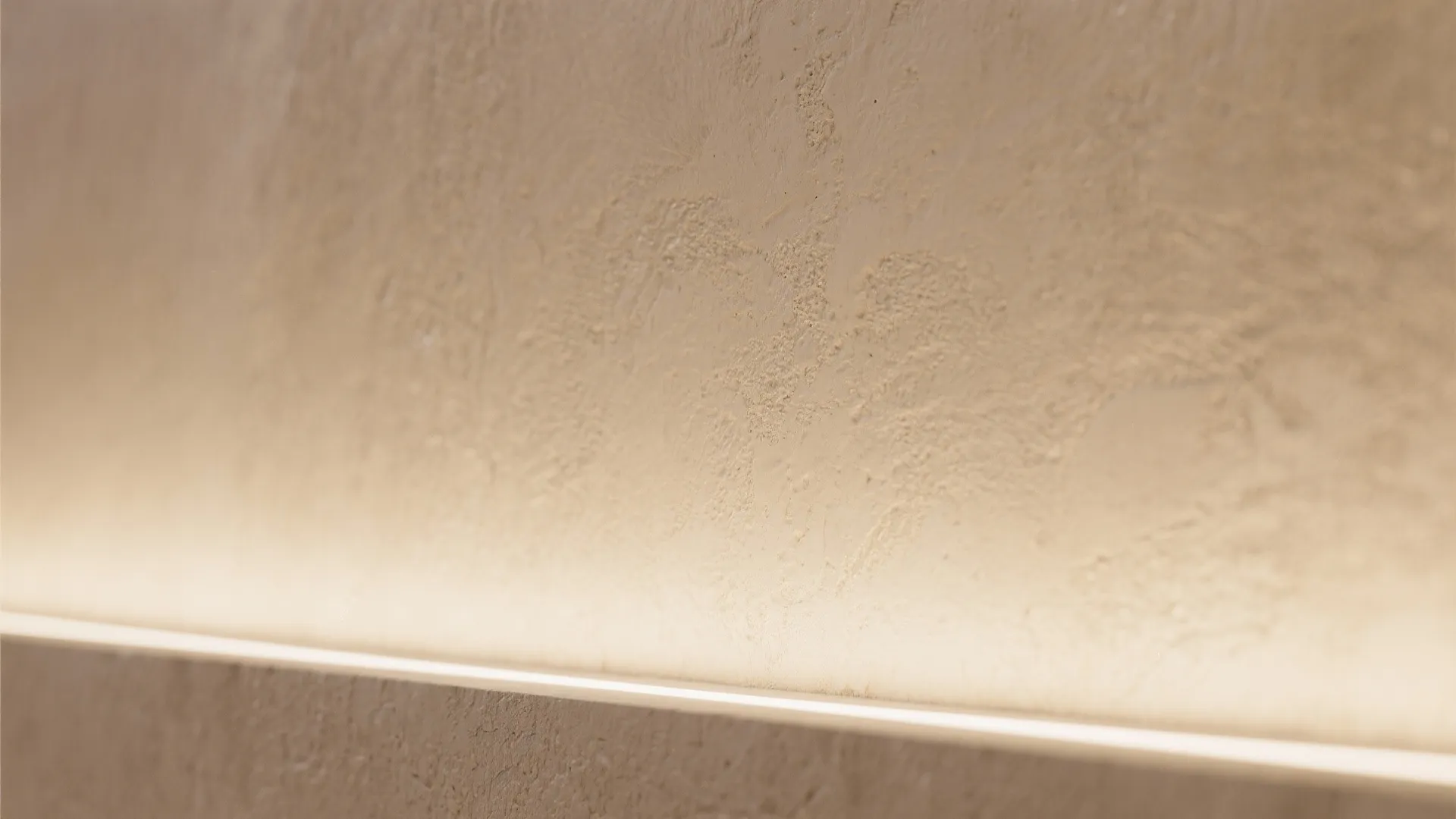 Close up of a textured beige wall with warm light shining from a hidden bottom strip