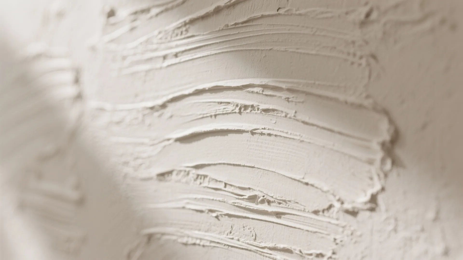 Close view of textured cream wall plaster showing smooth hand applied strokes and soft shadows