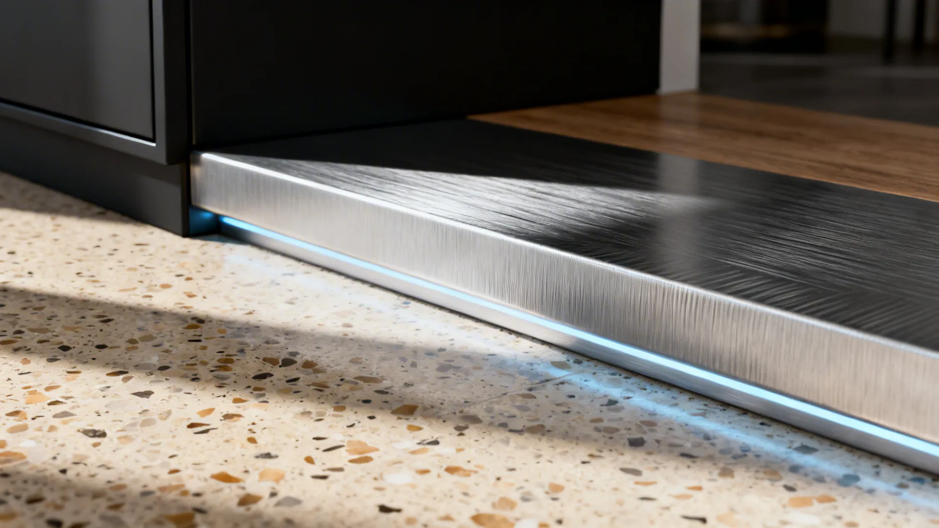 Modern kitchen cabinet base with brushed metal finish and blue LED light on terrazzo floor