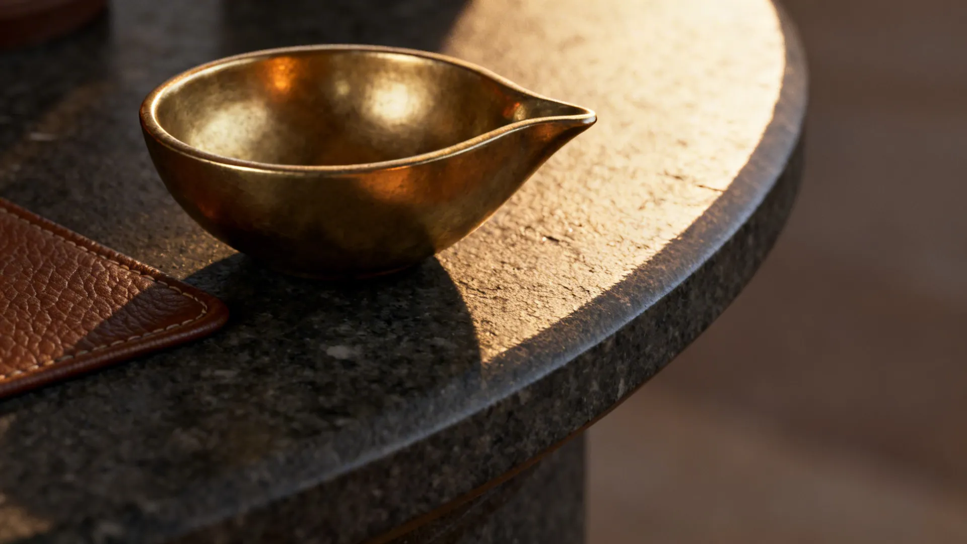Macro of honed basalt edge with a brushed brass diya and soft grazing light.