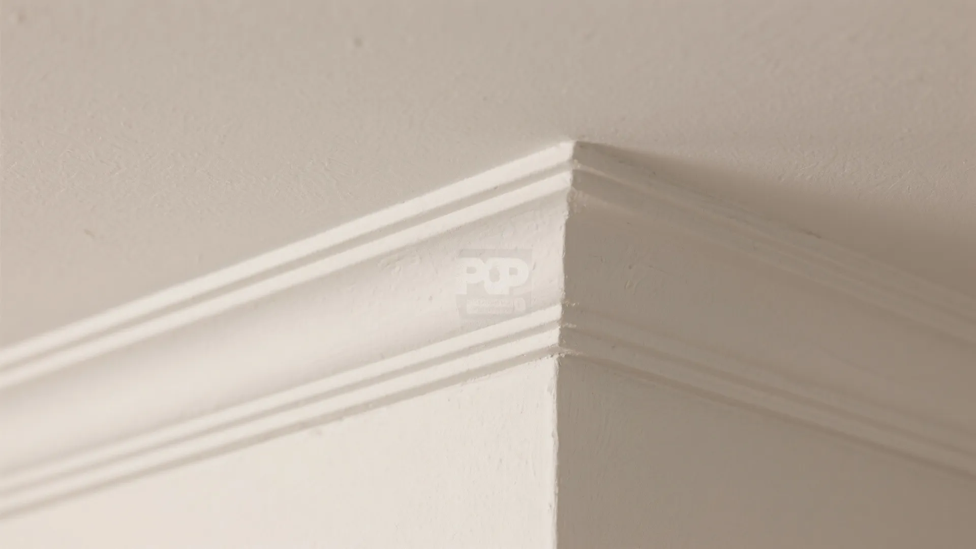 Close up view of a white ceiling corner showing simple decorative plaster molding and smooth finish