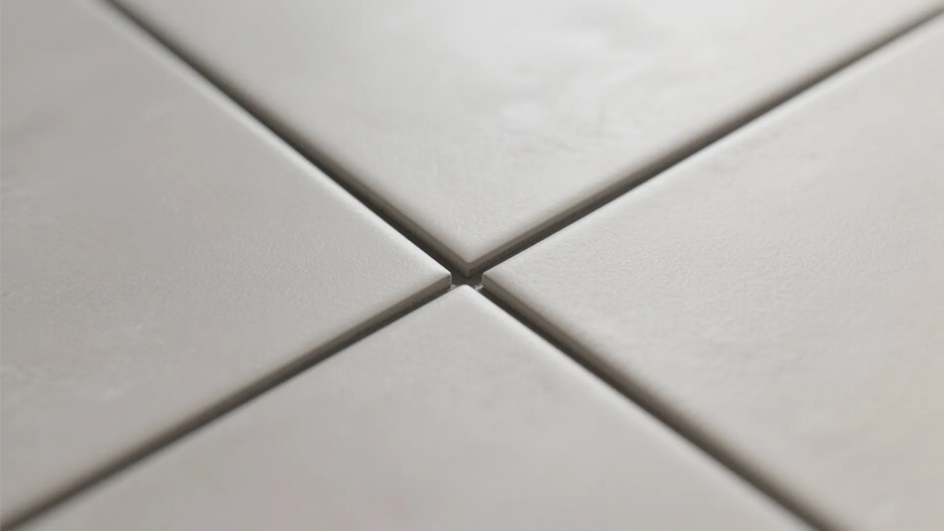 Close up view of white floor tiles meeting at a clean cross joint with grey grout