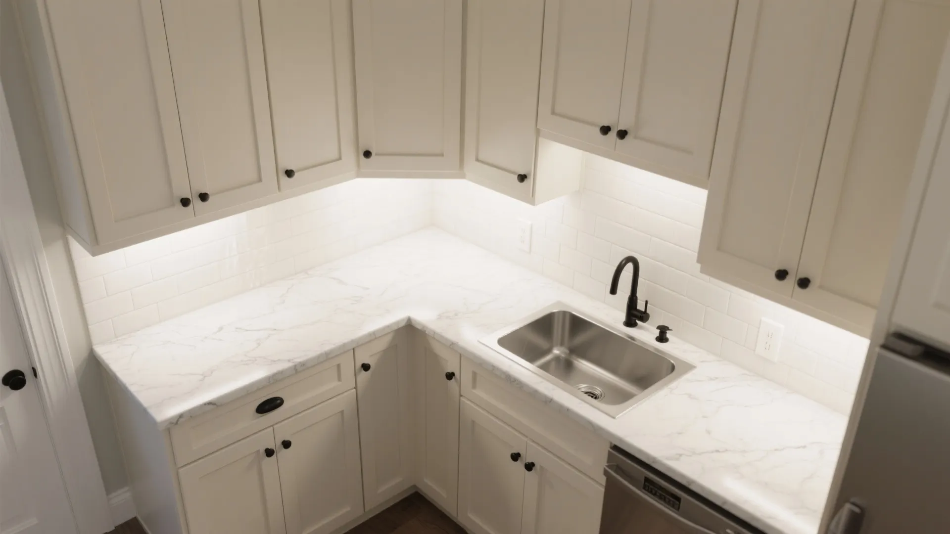 Top-down view of compact L-shaped kitchen with putty shaker cabinets, light quartz countertop, and matte black hardware.