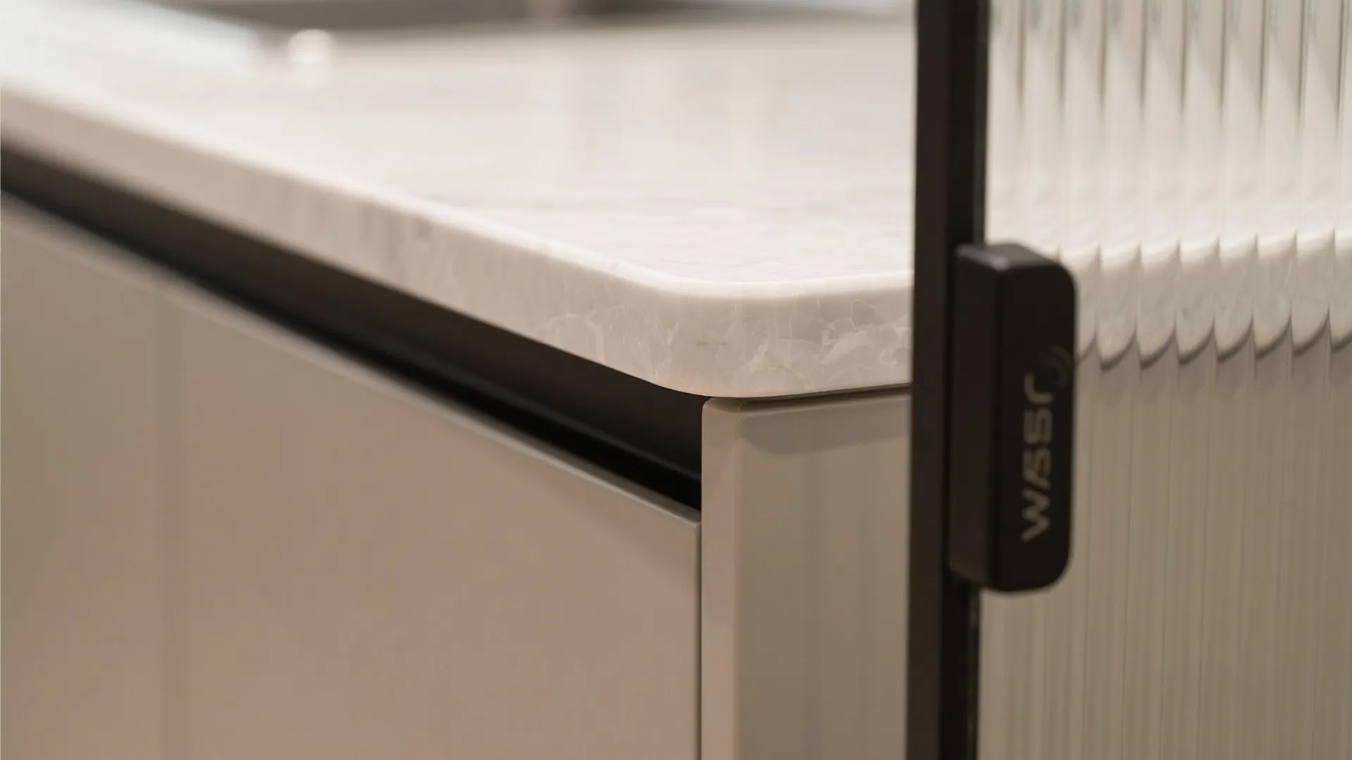 Close up view of a white marble kitchen counter edge and a ribbed glass door