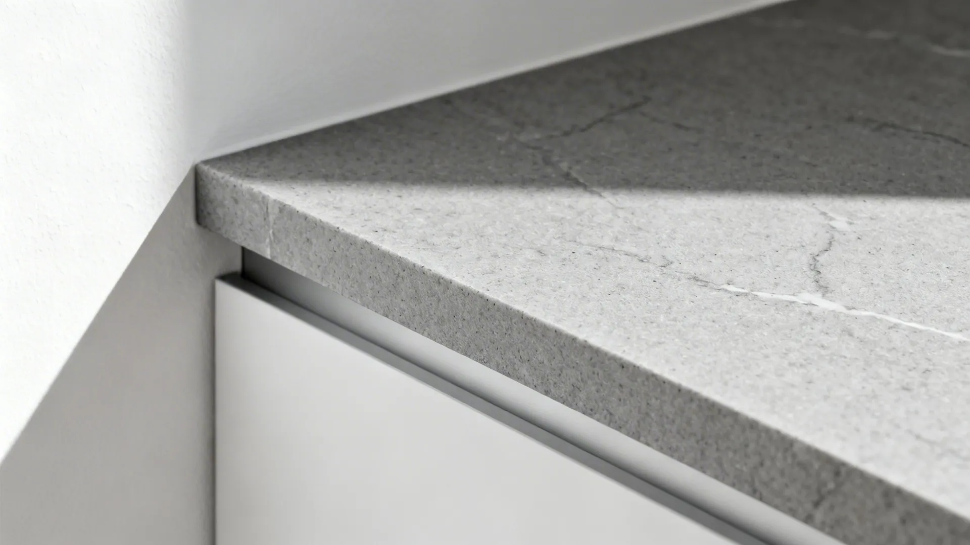Macro of honed grey quartz with a thin-profile edge beside a white wall.