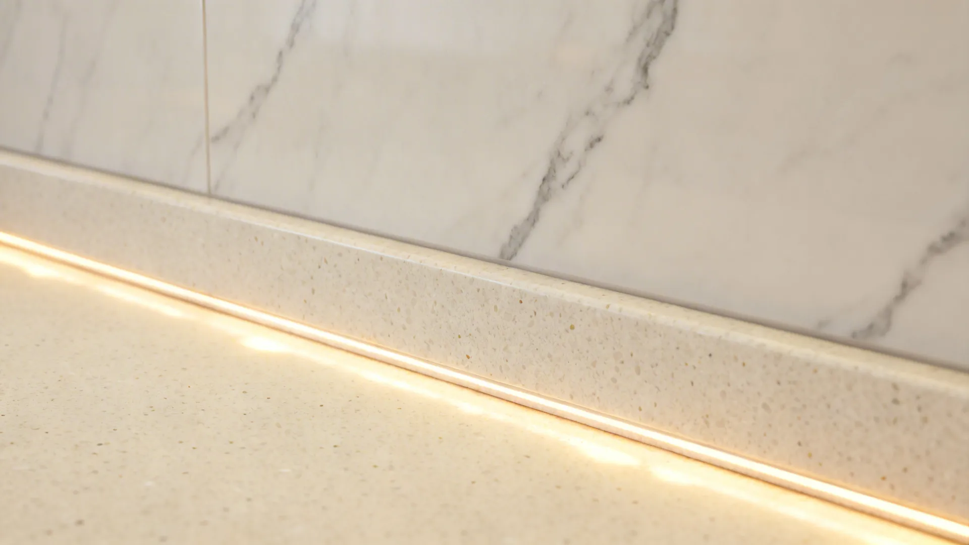 Macro view of honed warm-white quartz with faint veining at the counter-to-backsplash seam.