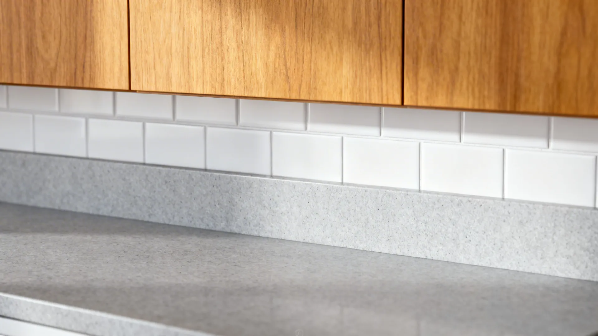 Honed gray quartz countertop with white subway tile and honey oak cabinets, highlighting material contrast.