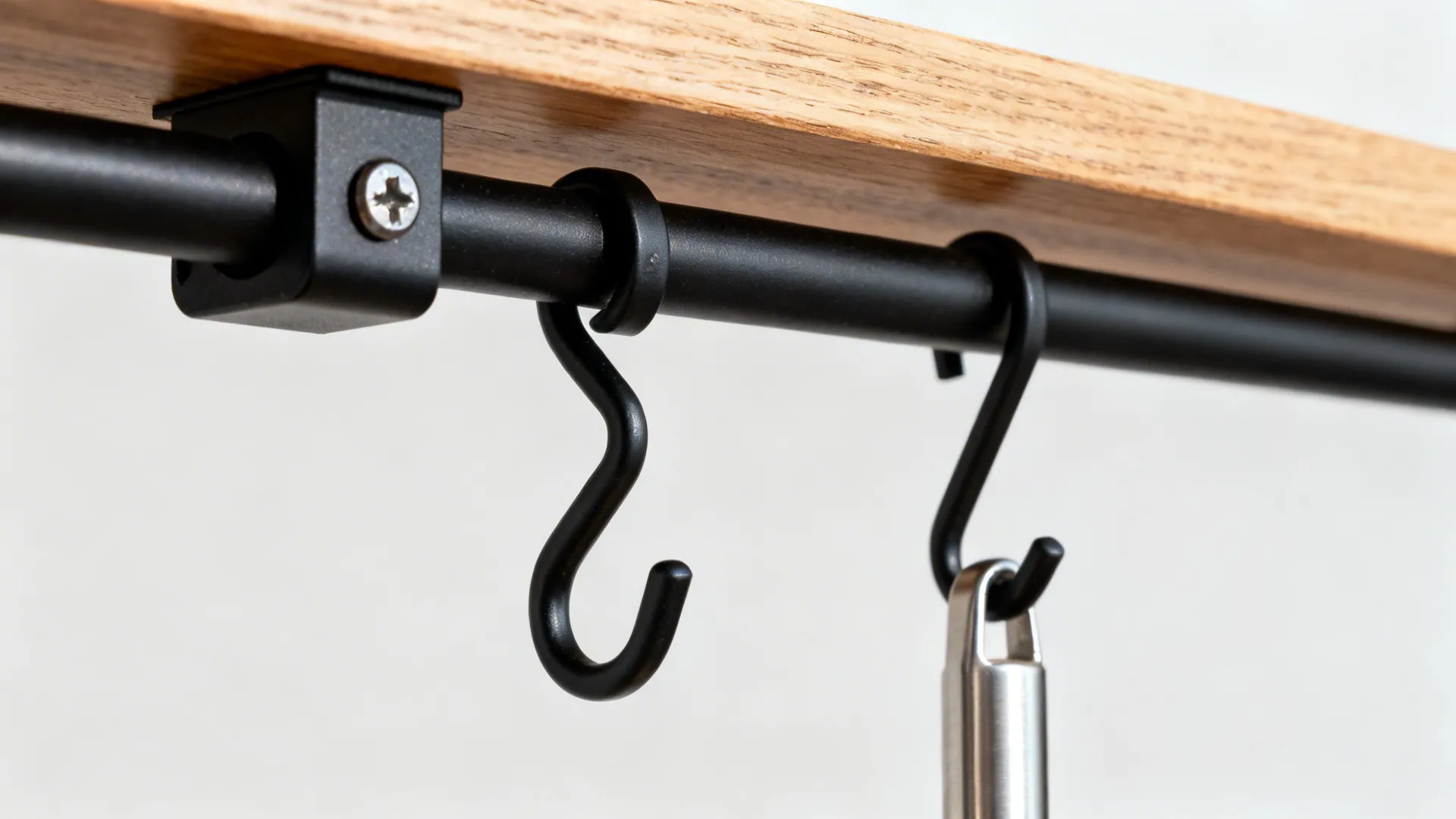 Close-up of matte black rail with S-hook and the edge of a narrow oak ledge.