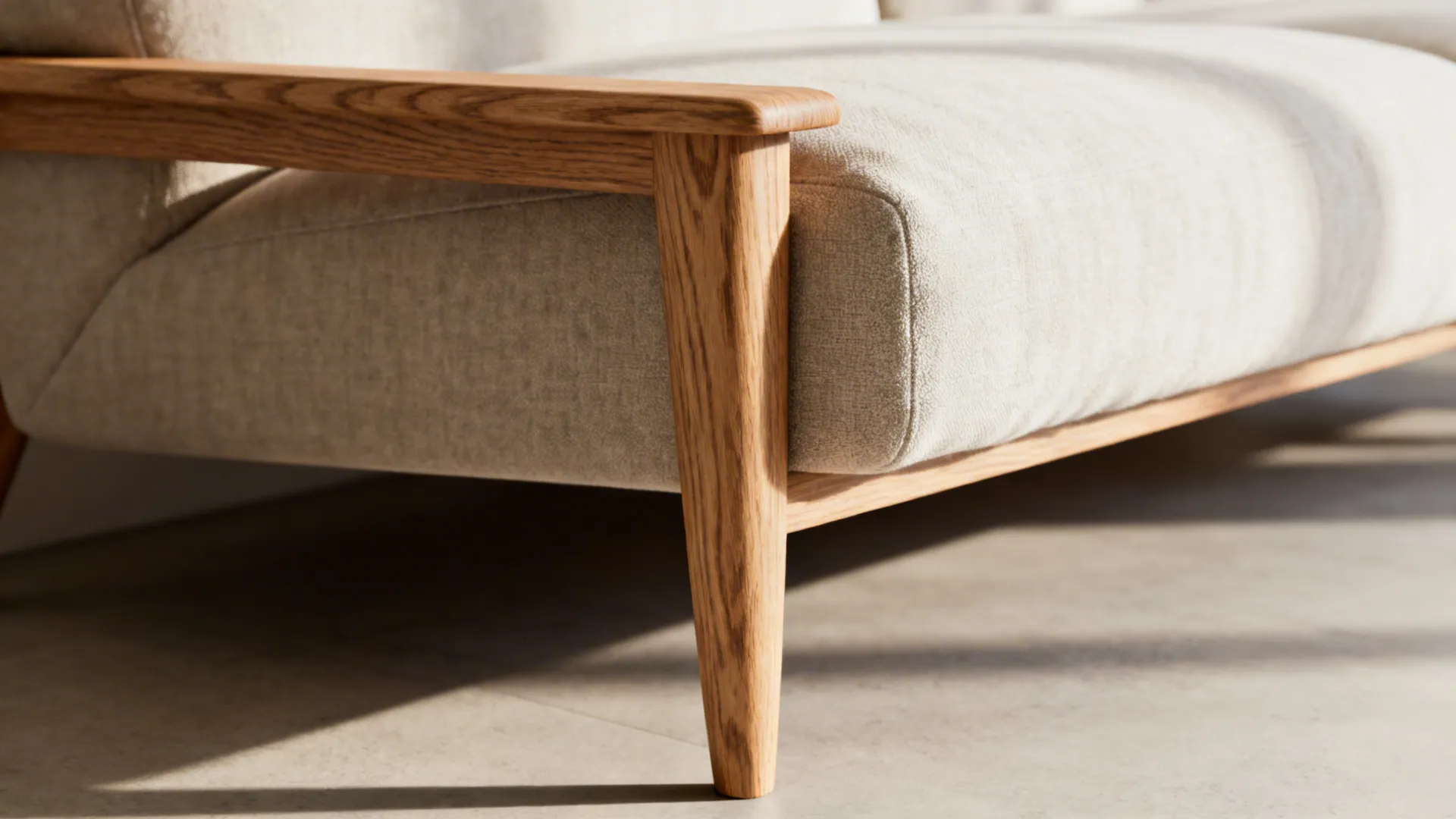 Close-up of a slim wooden sofa arm and tapered elevated leg showing wood grain and cushion edge.