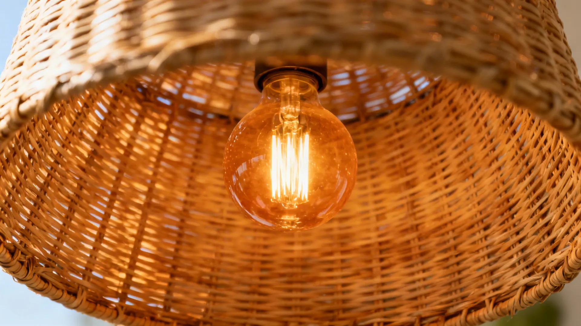 Warm glowing light bulb seen through the texture of a woven wooden basket ceiling light fixture