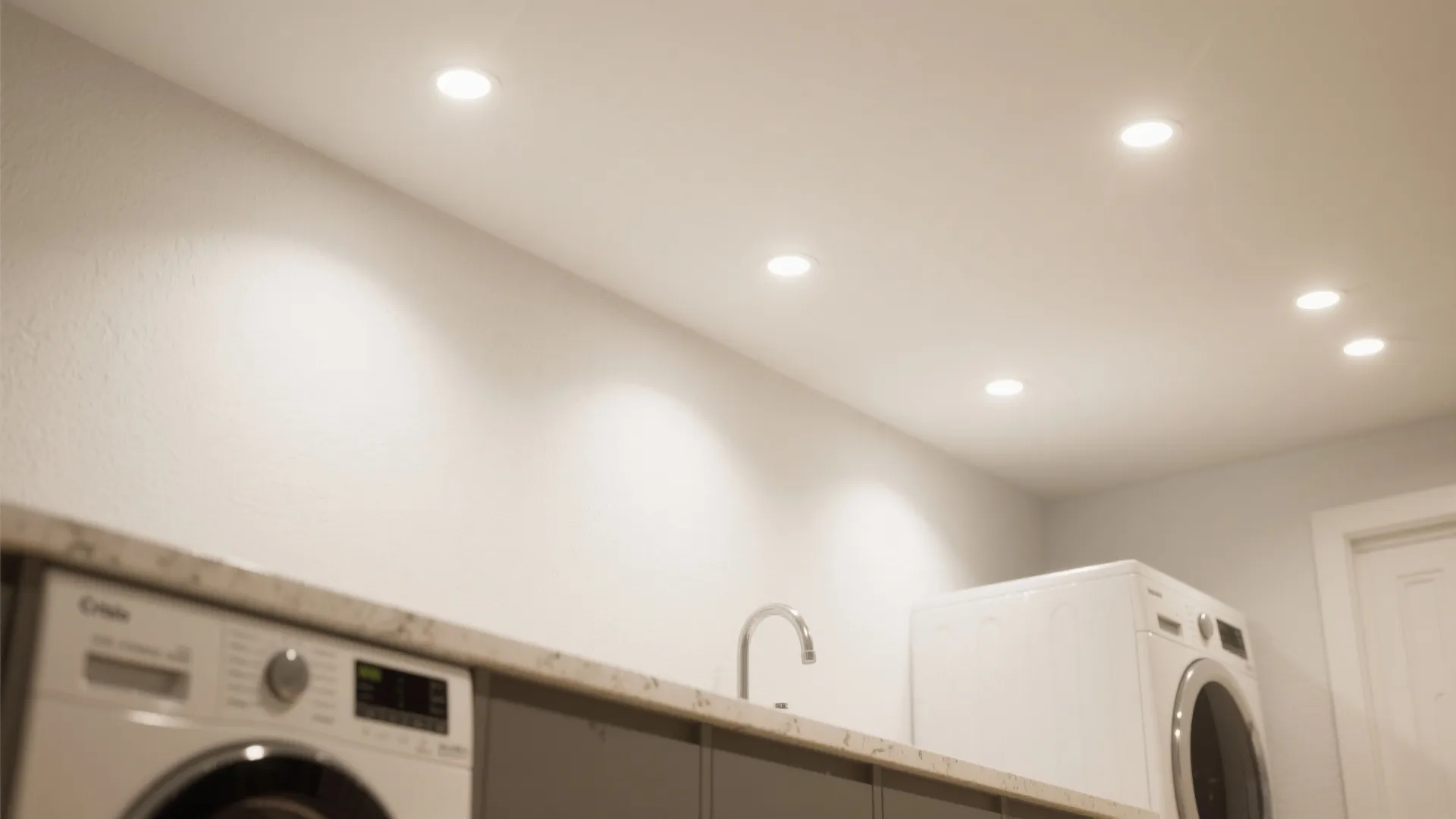 Close up view of bright ceiling light fixtures over a washing machine and countertop area
