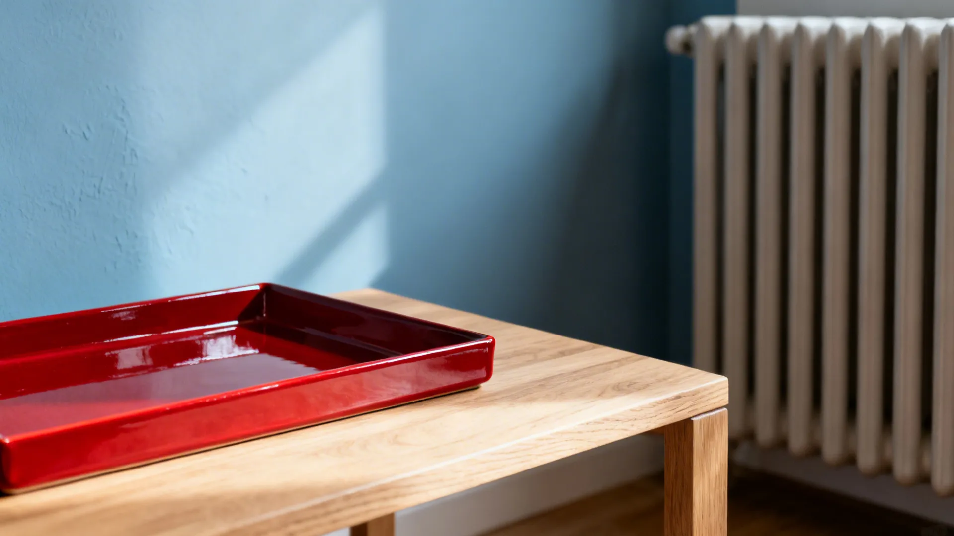Macro of glossy red tray against a matte muted blue wall and radiator with soft light.
