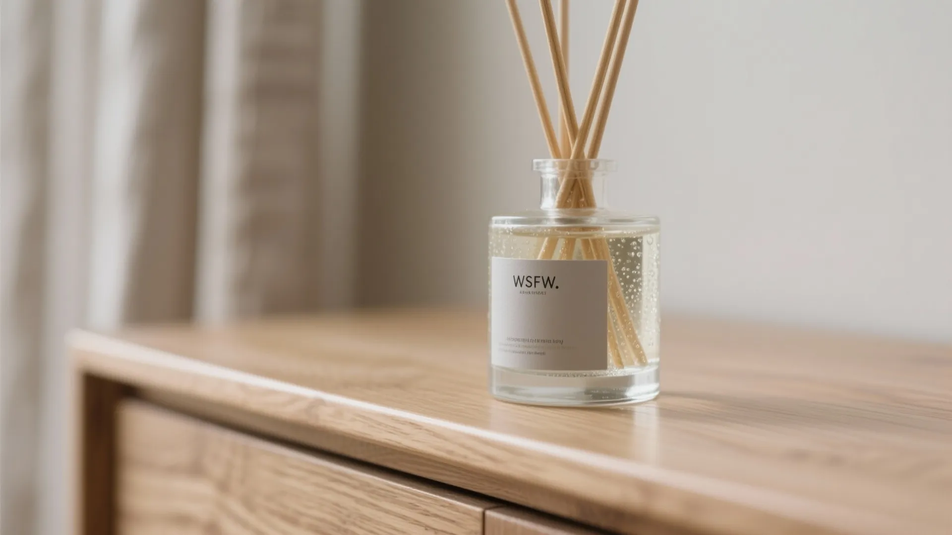 Macro of glass reed diffuser with rattan reeds on an oak console.