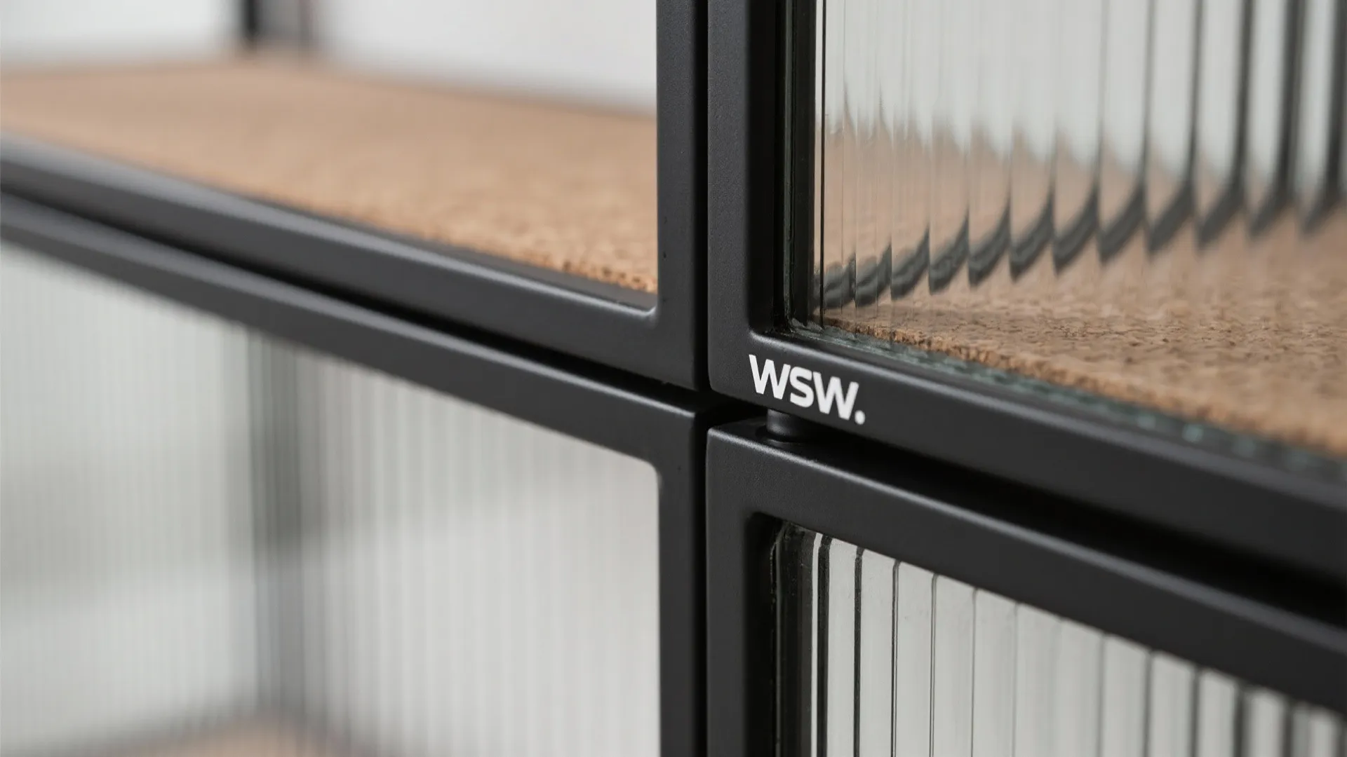 Close up view of black metal cabinet frame with textured glass panels and cork shelf