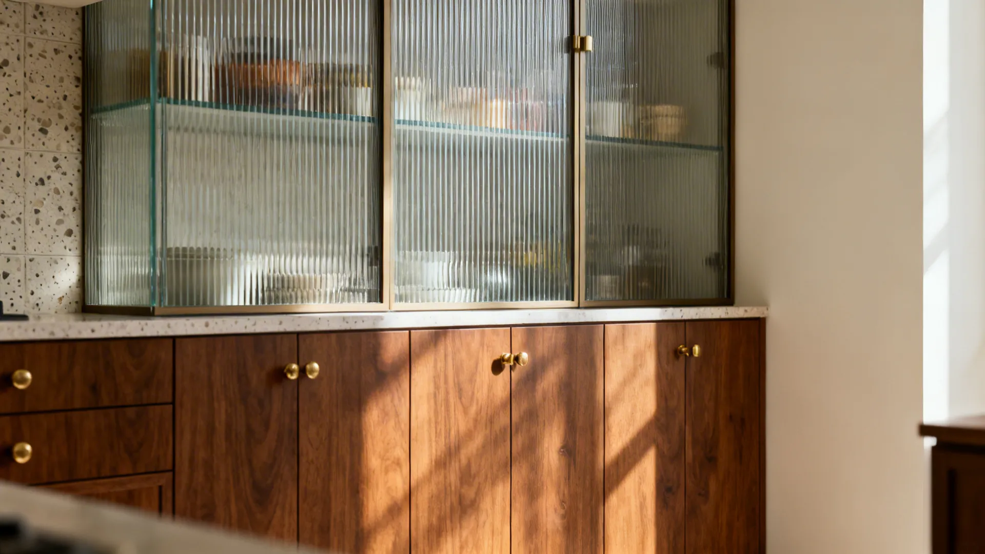 Compact kitchen with reeded glass upper cabinets, warm wood lowers, and brass hardware.