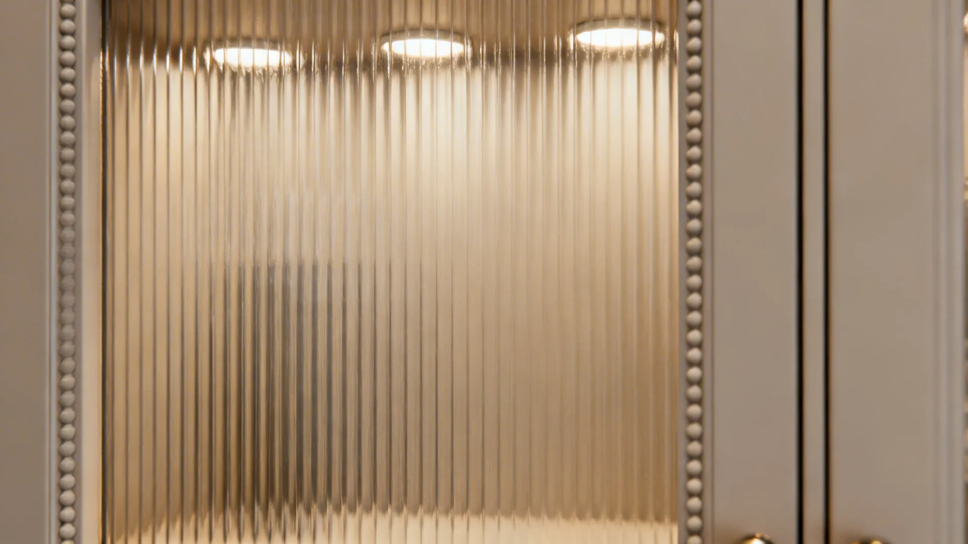 Macro of reeded cabinet glass softly diffusing interior light within a slim beaded frame.