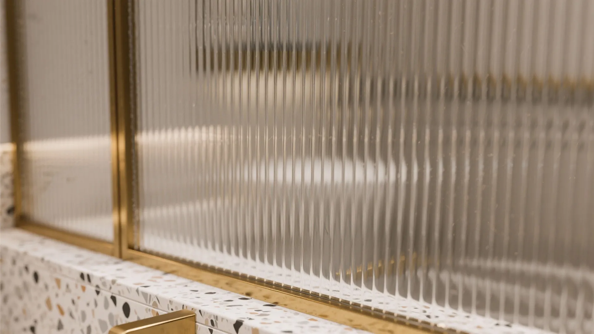 Macro view of reeded bathroom window glass with warm brass trim and terrazzo detail.